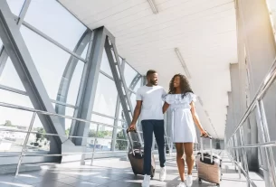 Casal de turista sorrindo com mala em aeroporto, pronta para uma viagem barata em 2025.
