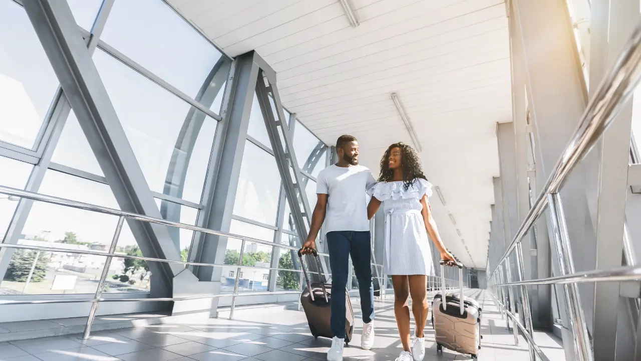Casal de turista sorrindo com mala em aeroporto, pronta para uma viagem barata em 2025.