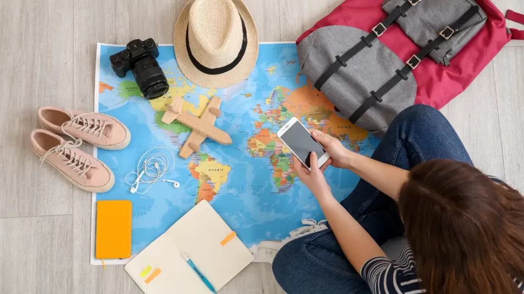 Mãos segurando celular, planejando uma viagem low-cost com mapa para 2025.