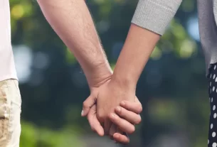 Duas mãos entrelaçadas contra um fundo neutro, representando confiança e vínculo em um relacionamento aberto.