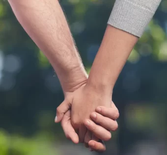 Duas mãos entrelaçadas contra um fundo neutro, representando confiança e vínculo em um relacionamento aberto.
