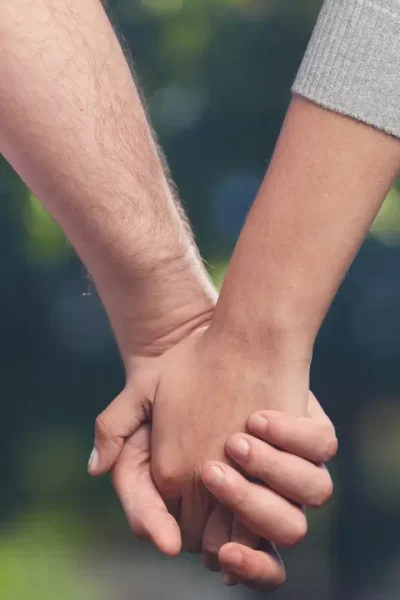 Duas mãos entrelaçadas contra um fundo neutro, representando confiança e vínculo em um relacionamento aberto.
