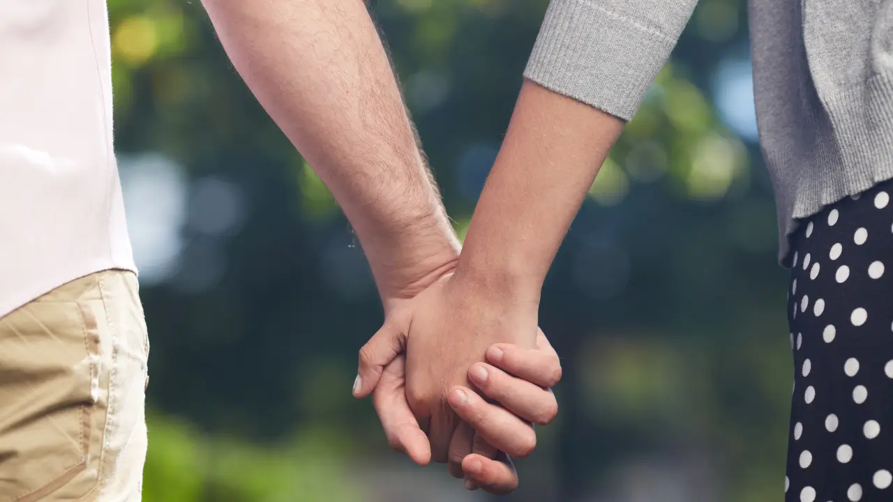 Duas mãos entrelaçadas contra um fundo neutro, representando confiança e vínculo em um relacionamento aberto.