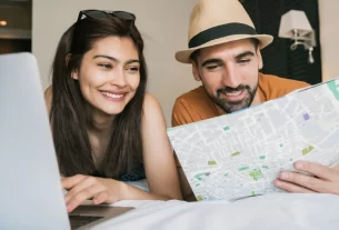 Casal sorrindo em frente a um mapa, planejando as férias em casal com tranquilidade e conexão.