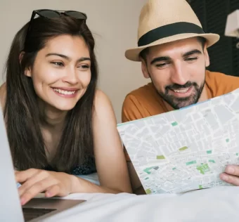 Casal sorrindo em frente a um mapa, planejando as férias em casal com tranquilidade e conexão.