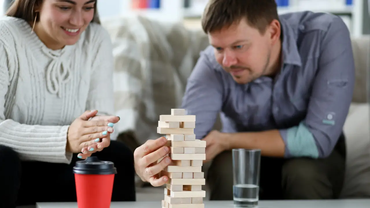 Casal construindo uma pequena torre de blocos de madeira, simbolizando a construção da relação e o amor dradouro
